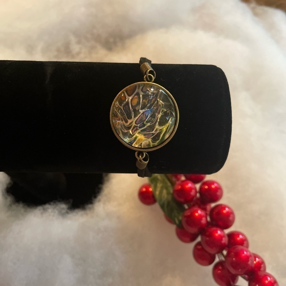 Hand painted acrylic design on glass bracelet.  Attached to metal.  Adjustable